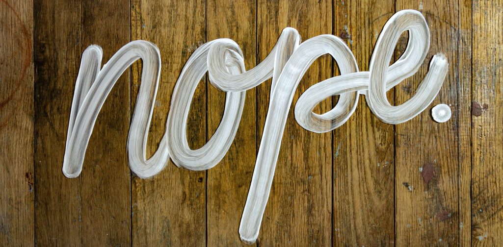 In großen, klaren Buchstaben steht "nope." auf einem Holzuntergrund.